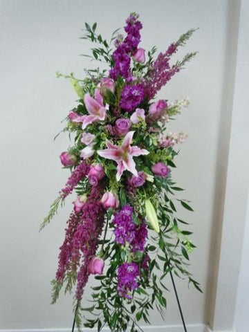 Funeral arrangement on the holder  with purple roses, lilies and delphinium.