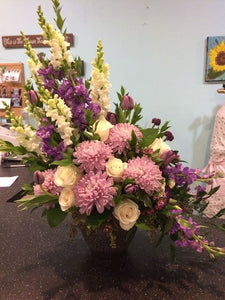 This stunning arrangement of purple sider chysanthemums and lavender snapdragons will express your sympathy lovingly and tastefully.  Includes:   Lavender snap dragons, white roses, lavender spider chrysanthemums with assorted greenery. Delivered in a basket or vase. Free message card