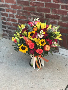 Warm their hearts and brighten their table with this lush fall bouquet, arranged in glass vase.  Includes:  Sunflowers, pink roses, orange chrysanthemums, yellow lilies and snap dragons, assorted greens. Artificial pumpkins and apples. Vase Free message card