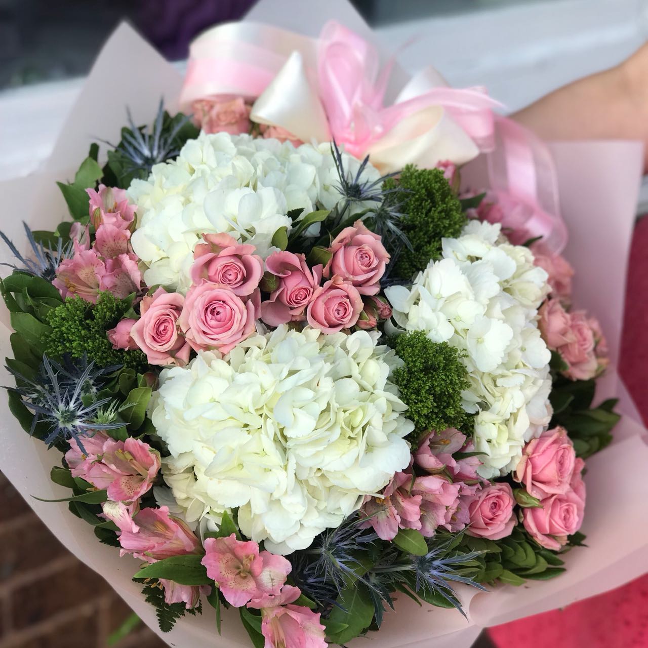 Would you walk a mile for one of her smiles? You can bet she'll be walking toward you, arms outstretched, when she receives this gorgeous. And wait till you see the smile she gives you.  Includes:  White hydrangea, pink mini roses, pink alstroemeria, eringium, assorted greens. Free message card
