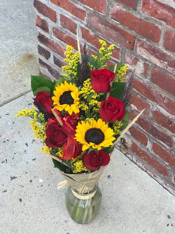 A gift of pure joy!  You know someone who could use a lift. Give it to them the easy way. Just give us a click.  Includes:  Red roses, sunflowers, solidago,assorted greens. Free message card