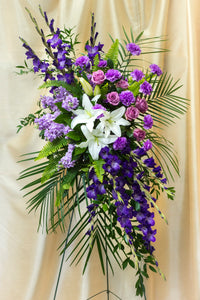 Funeral arrangement on a holder of lilies, purple stock, gladiolus and roses.